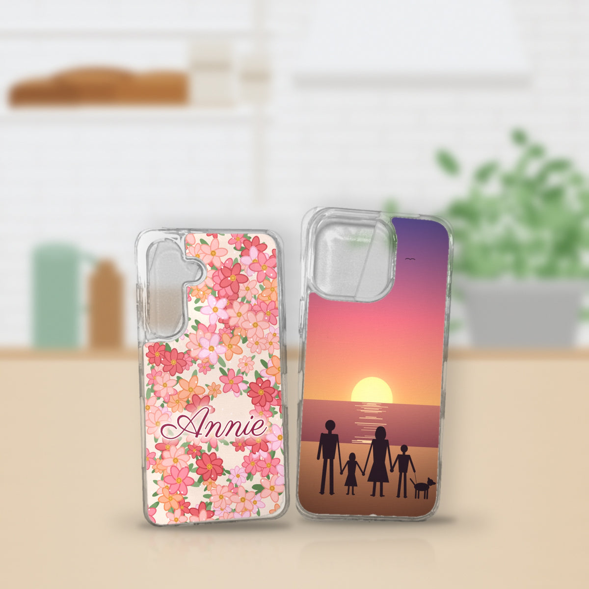 Two custom printed clear phone cases – a floral design with the name Annie and a family sunset scene – on a kitchen bench